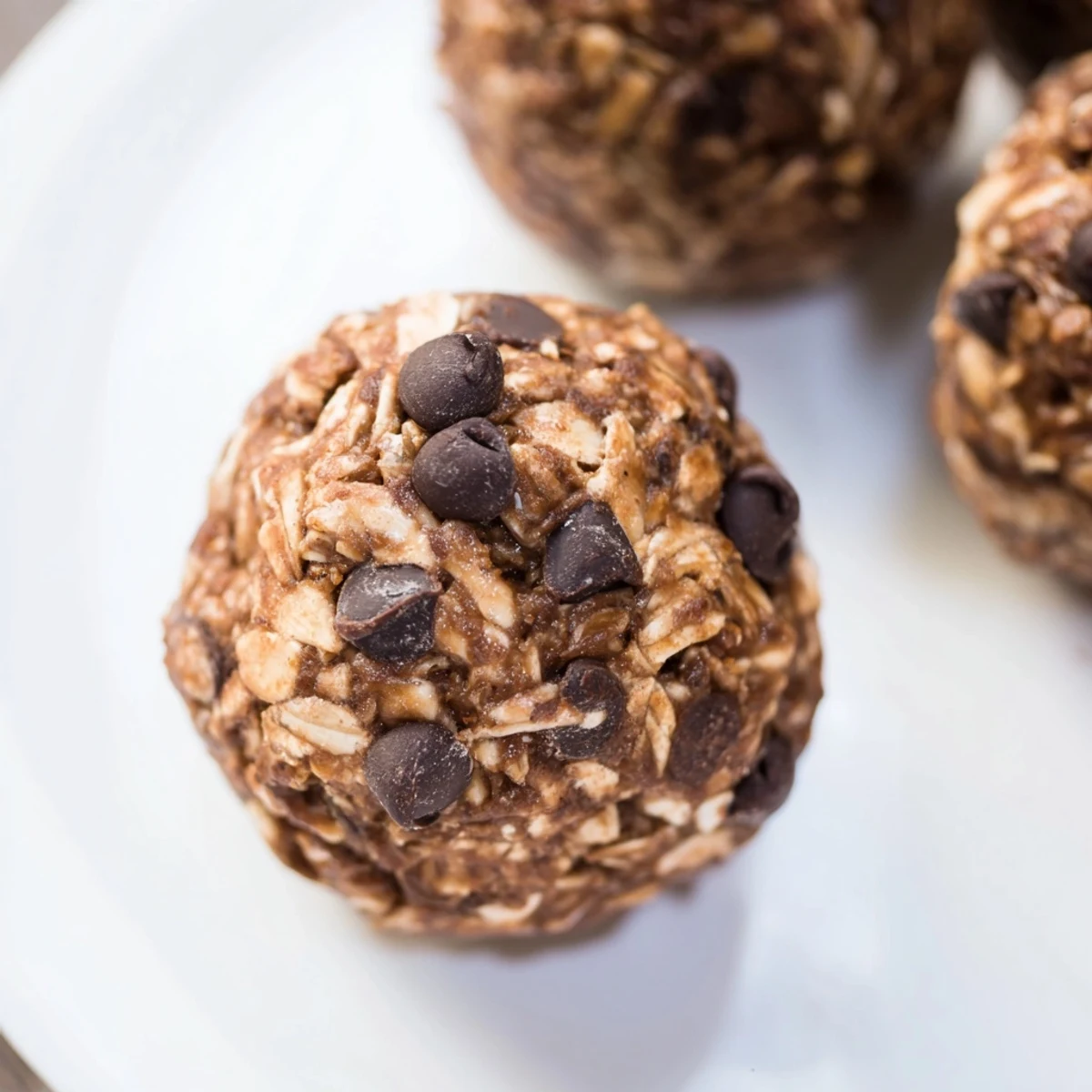 These Chocolate Peanut Butter Energy balls are stacked on a small white plate with a glass of almond milk in the background.