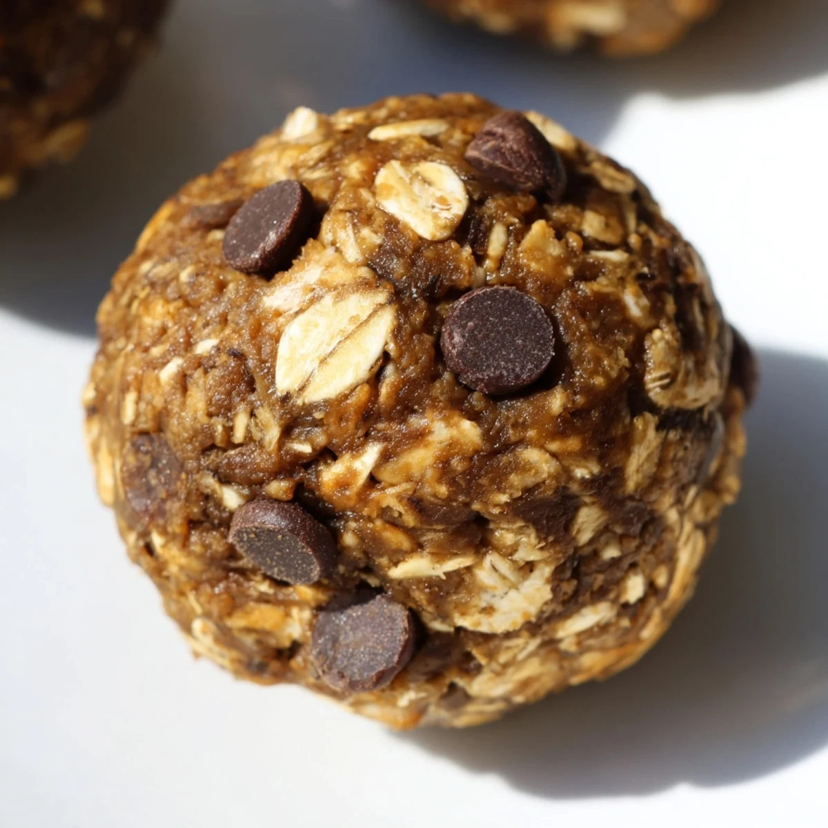 A single Chocolate Peanut Butter Energy ball is split in half, revealing oats, chocolate chips, and a sticky texture on a marble surface. 