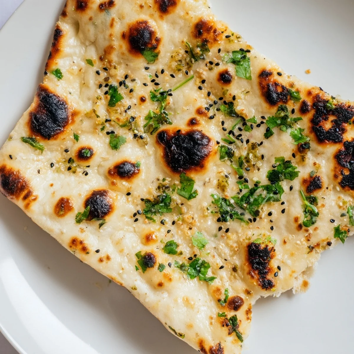 Golden-brown Garlic Naan Bread with Nigella Seeds resting on a wooden board, featuring soft bubbles and aromatic garlic butter ready to be torn.