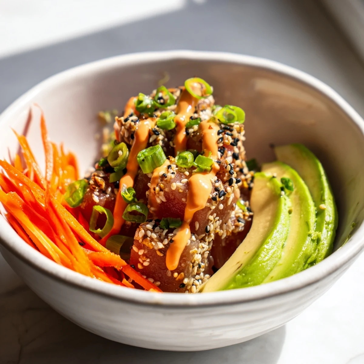 A close-up view of a Spicy Tuna Poke Bowl with Sriracha Mayo, featuring marinated tuna cubes, creamy avocado slices, and crisp julienned carrots atop a bed of white rice.