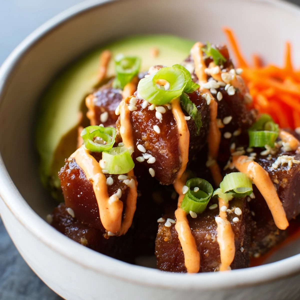 The finished Spicy Tuna Poke Bowl with Sriracha Mayo is garnished with sesame seeds and nori strips, with the vibrant pink sauce drizzled over fresh cucumbers and edamame.