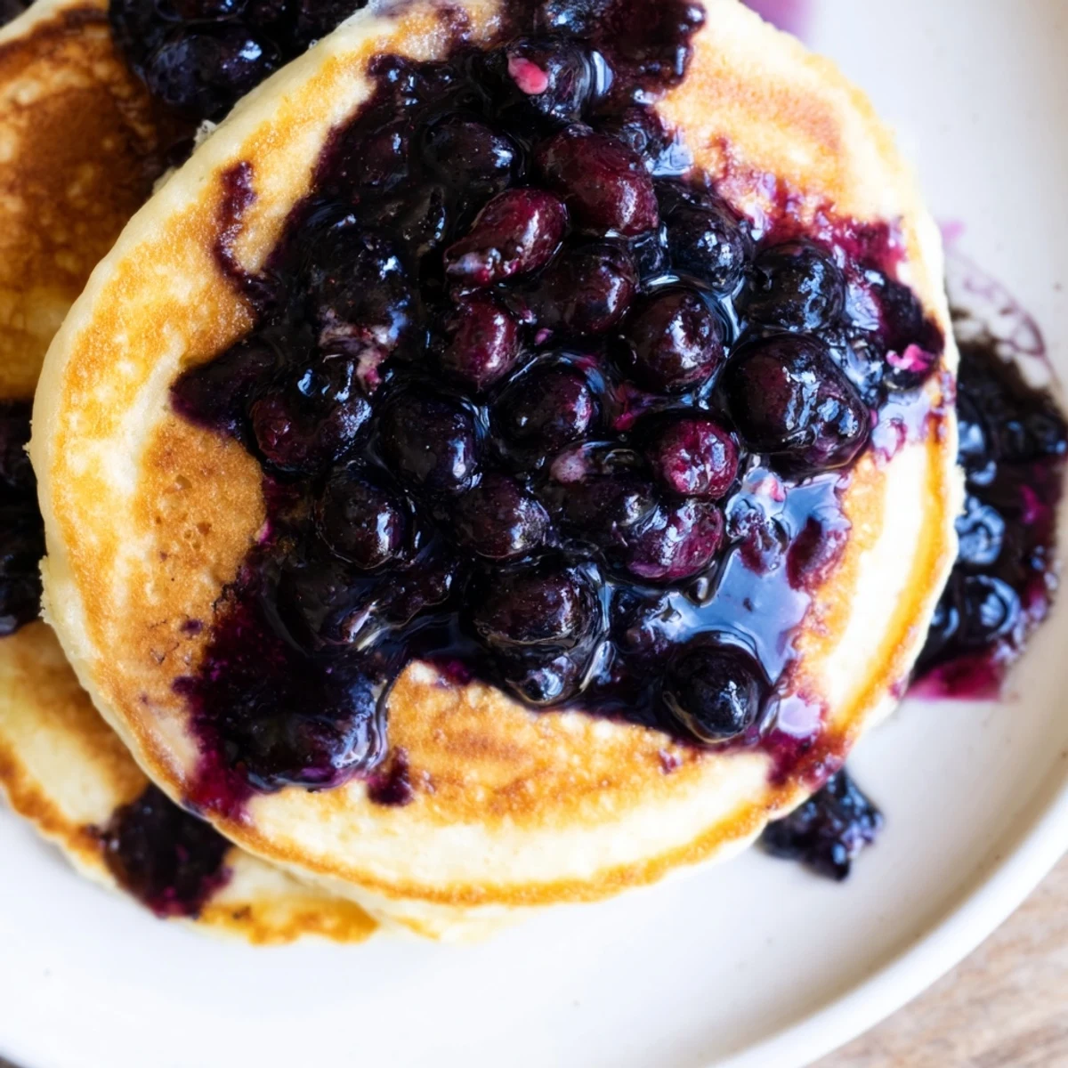 Golden-brown Lemon Ricotta Pancakes stacked high, generously drizzled with warm, velvety blueberry syrup for a sweet finish.