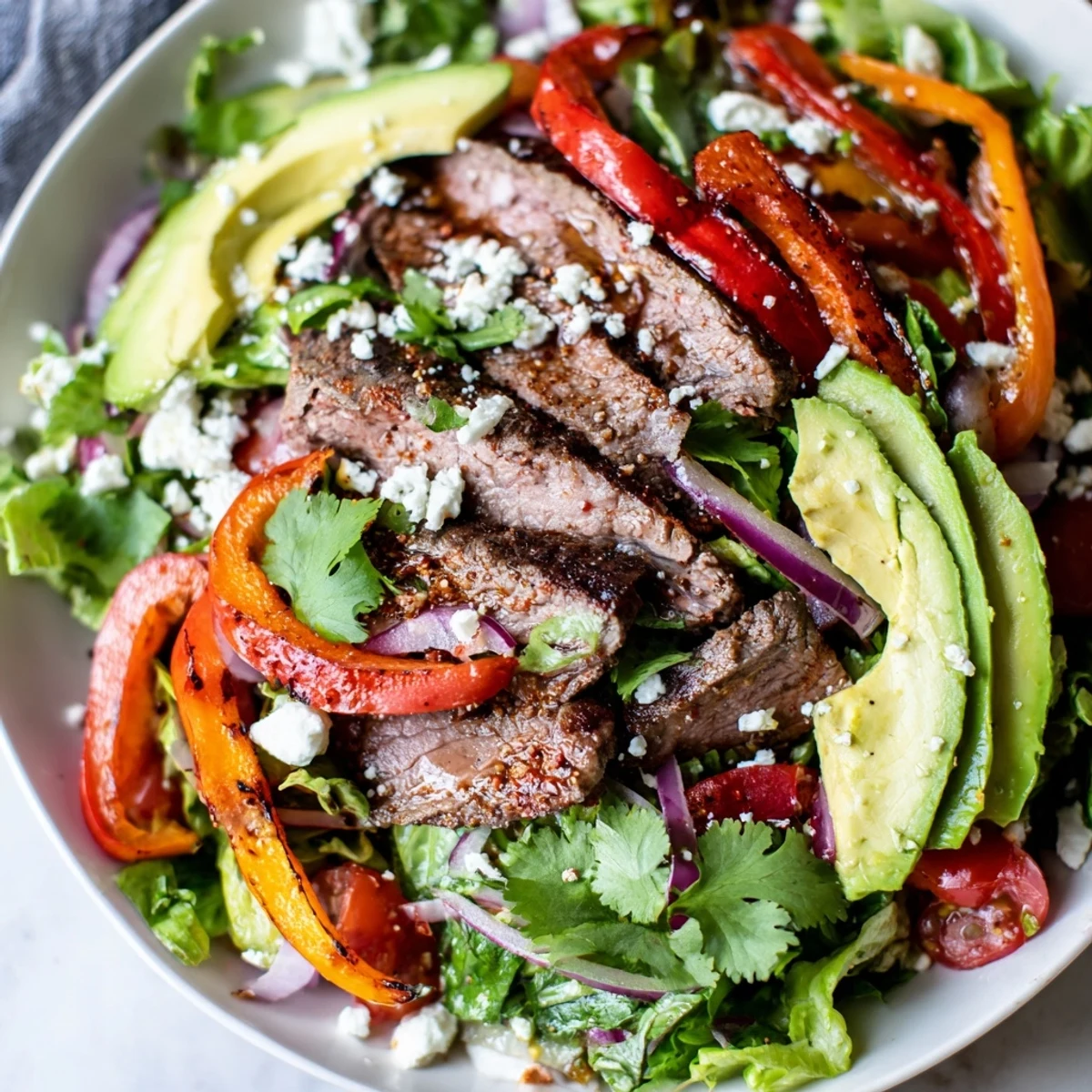 Sliced grilled beef strips rest on a bed of mixed greens, topped with vibrant sautéed peppers and onions in this Beef Fajita Salad.