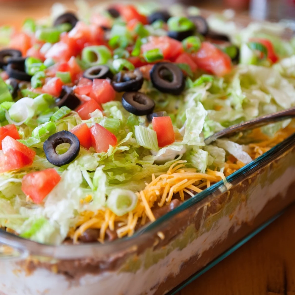 A close-up of End Zone Seven Layer Taco Dip with vibrant layers of beans, guacamole, and melted cheese, ready for dipping.