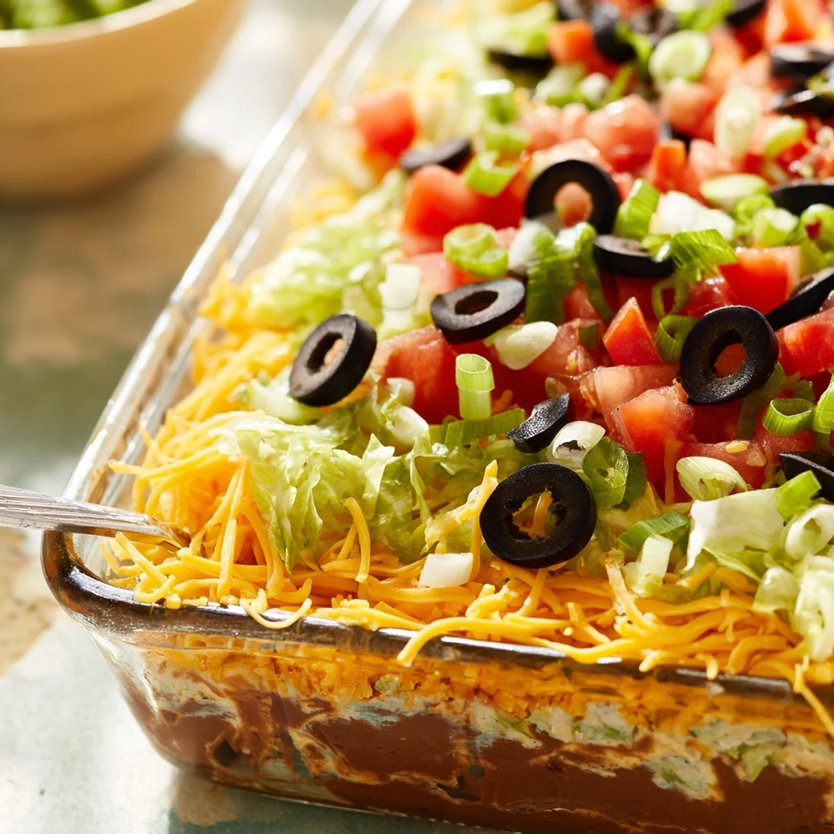 End Zone Seven Layer Taco Dip displayed in a glass dish, featuring distinct layers of refried beans, sour cream, and cheddar.