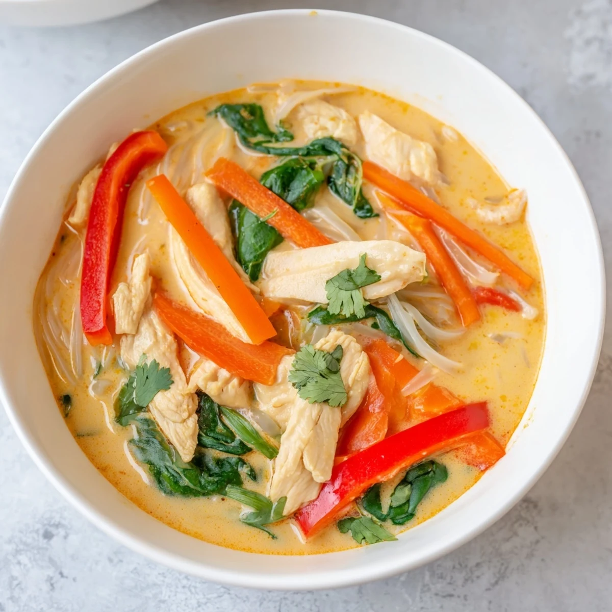 A warm bowl of Thai Red Curry Noodle Soup with Chicken, featuring tender chicken, rice noodles, and crisp vegetables in a creamy, aromatic broth.  