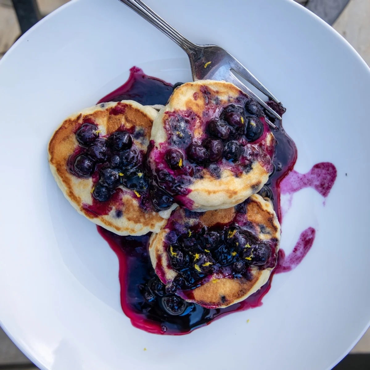 Fluffy lemon ricotta pancakes topped with warm, glossy blueberry syrup on a white plate.  
