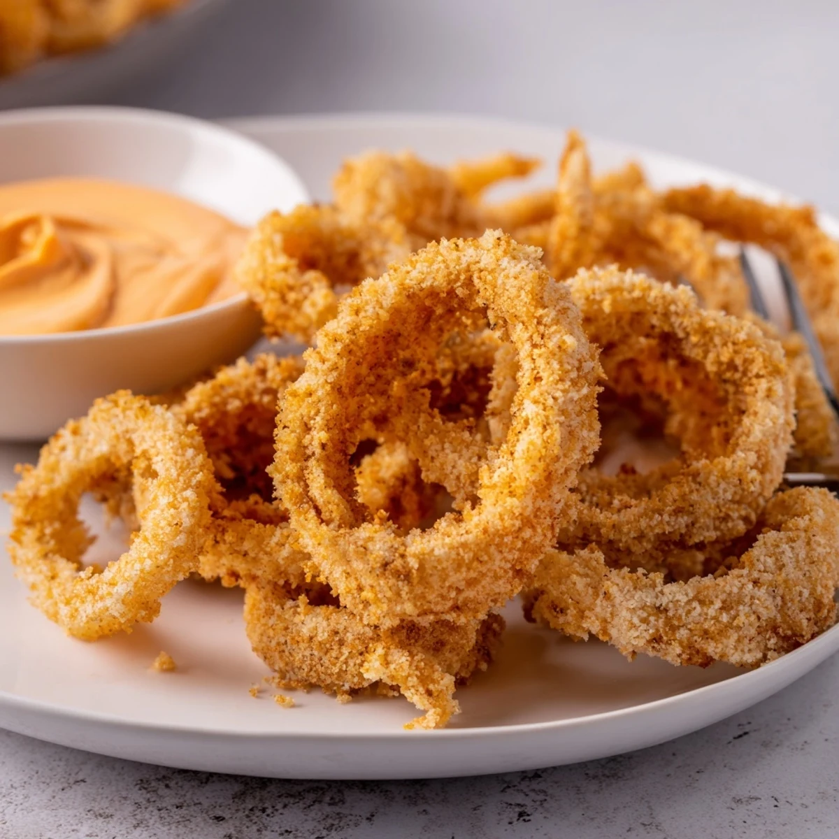 Golden, crispy air fryer onion rings piled high with creamy tangy dipping sauce ready to enjoy.