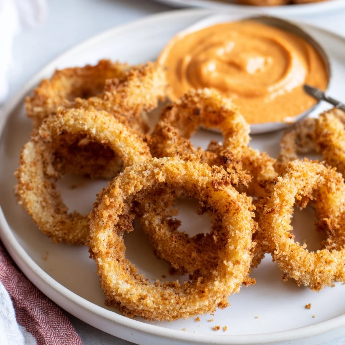 Sizzling hot air fryer onion rings stacked on a plate beside a small bowl of dip.
