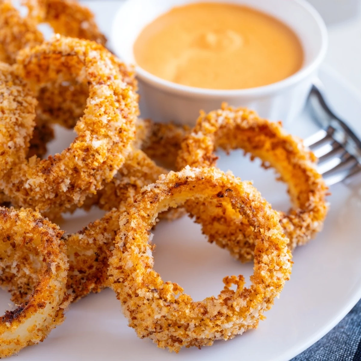 Freshly cooked air fryer onion rings showing golden brown crunch next to a creamy dipping sauce.