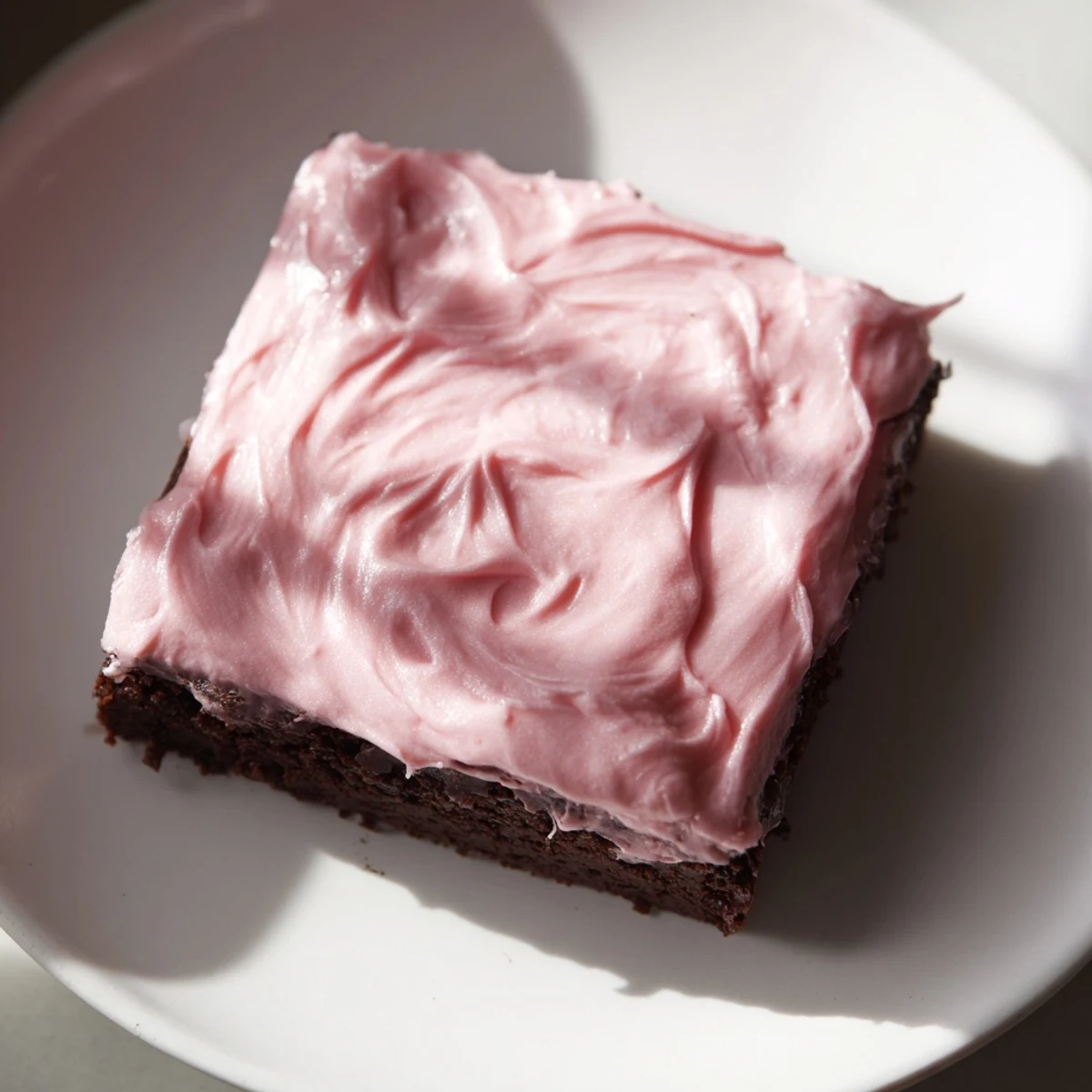 Neatly cut squares of Brownies with Pink Frosting arranged on a marble countertop, perfect for an afternoon treat.