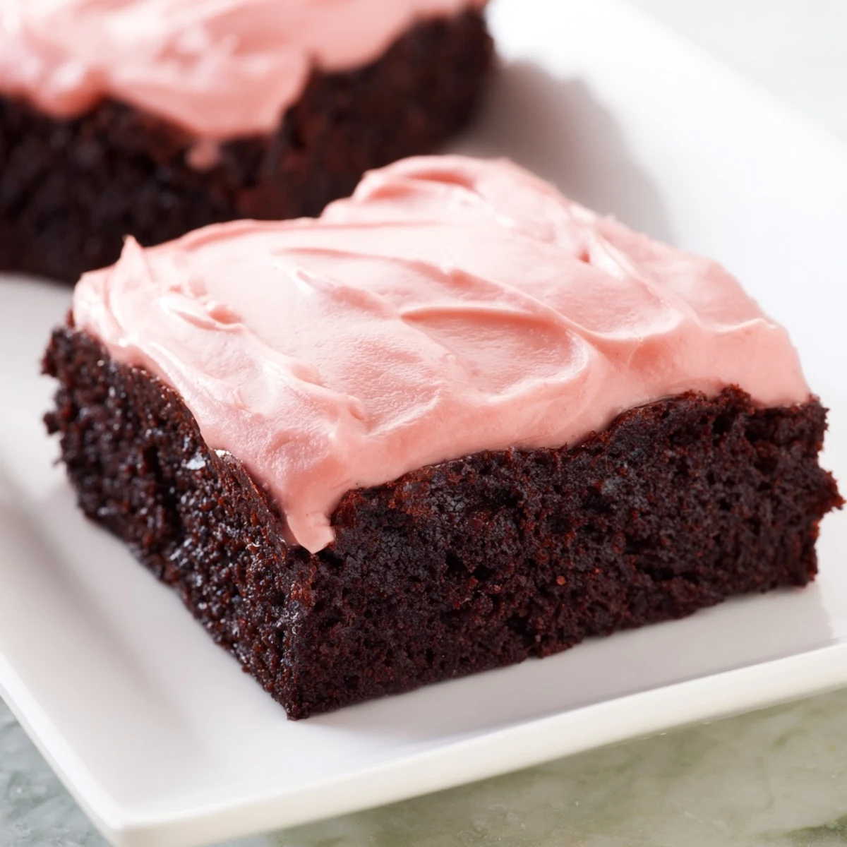 Fudgy homemade brownies with pink frosting are cut into squares on a marble counter, ready for a party.  