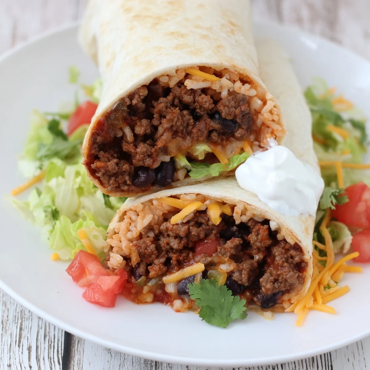 Golden-brown flour tortilla stuffed with seasoned ground beef, creamy black beans, fluffy rice, melted cheddar, and fresh lettuce and tomato, served on a white plate.  