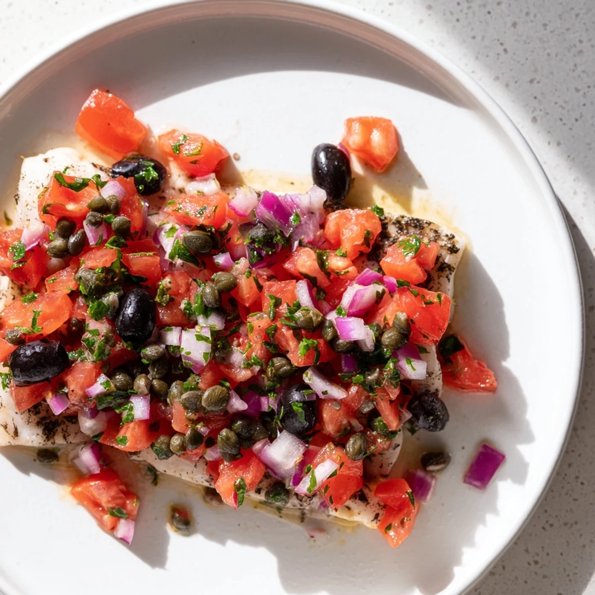 Tender baked cod with a zesty tomato and olive salsa, served on a white plate.