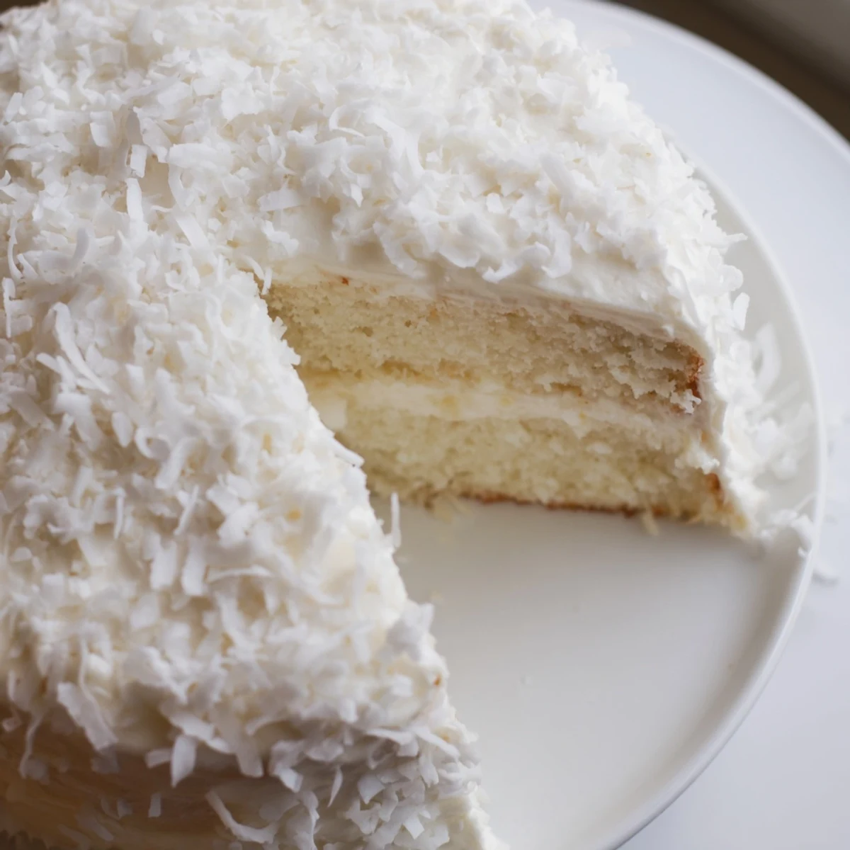 Moist layers of Easter Coconut Cake with rich cream cheese frosting, finished with fluffy coconut flakes and colorful spring candies for serving.
