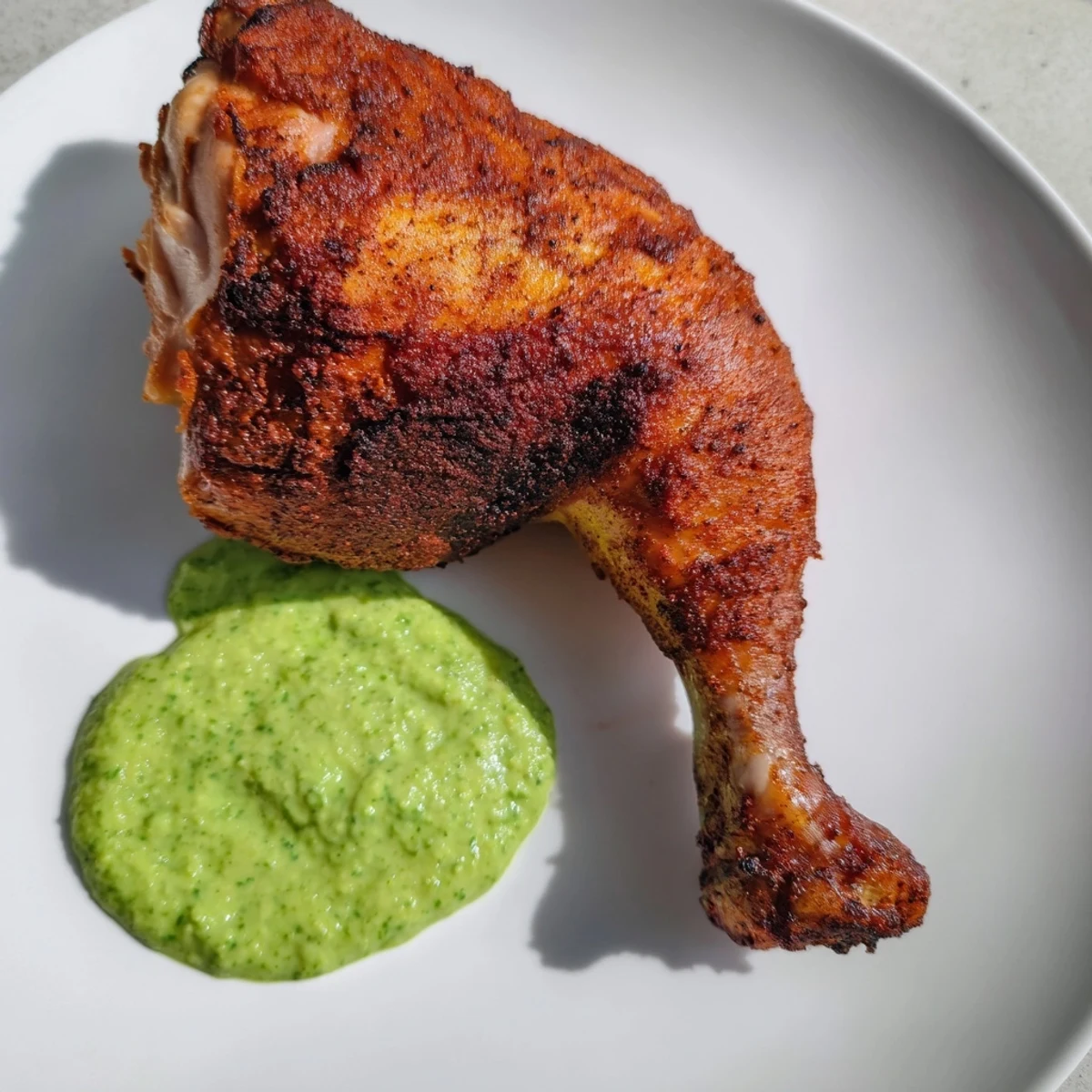 A close-up of Peruvian Roast Chicken with Creamy Green Sauce highlights the herb-flecked sauce in a bowl, garnished with fresh cilantro and lime wedges.