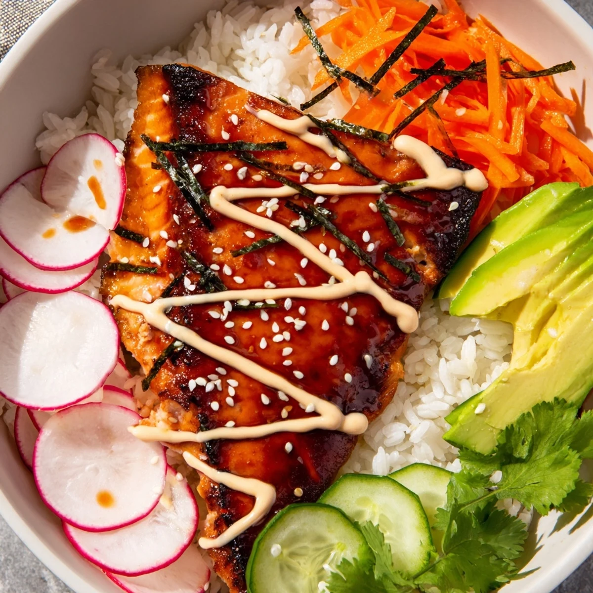 A fork lifts flaky teriyaki salmon from a bed of rice topped with avocado and zesty sriracha mayo.