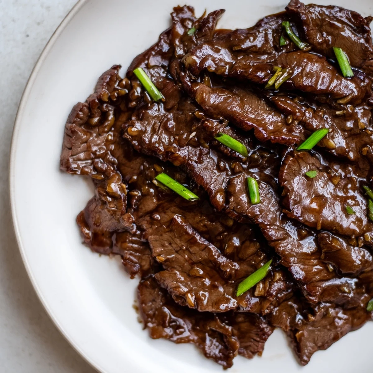 Steamed jasmine rice and green onions perfectly accompany Ultimate Slow Cooker Mongolian Beef served on a dinner plate.