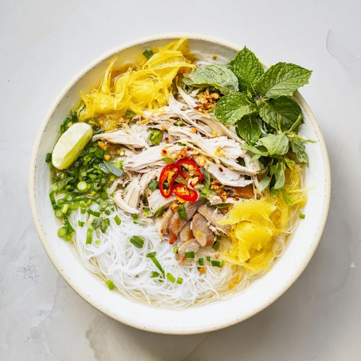 Fragrant Bun Thang soup topped with pork sausage, fresh herbs, and lime wedges on a wooden table.  