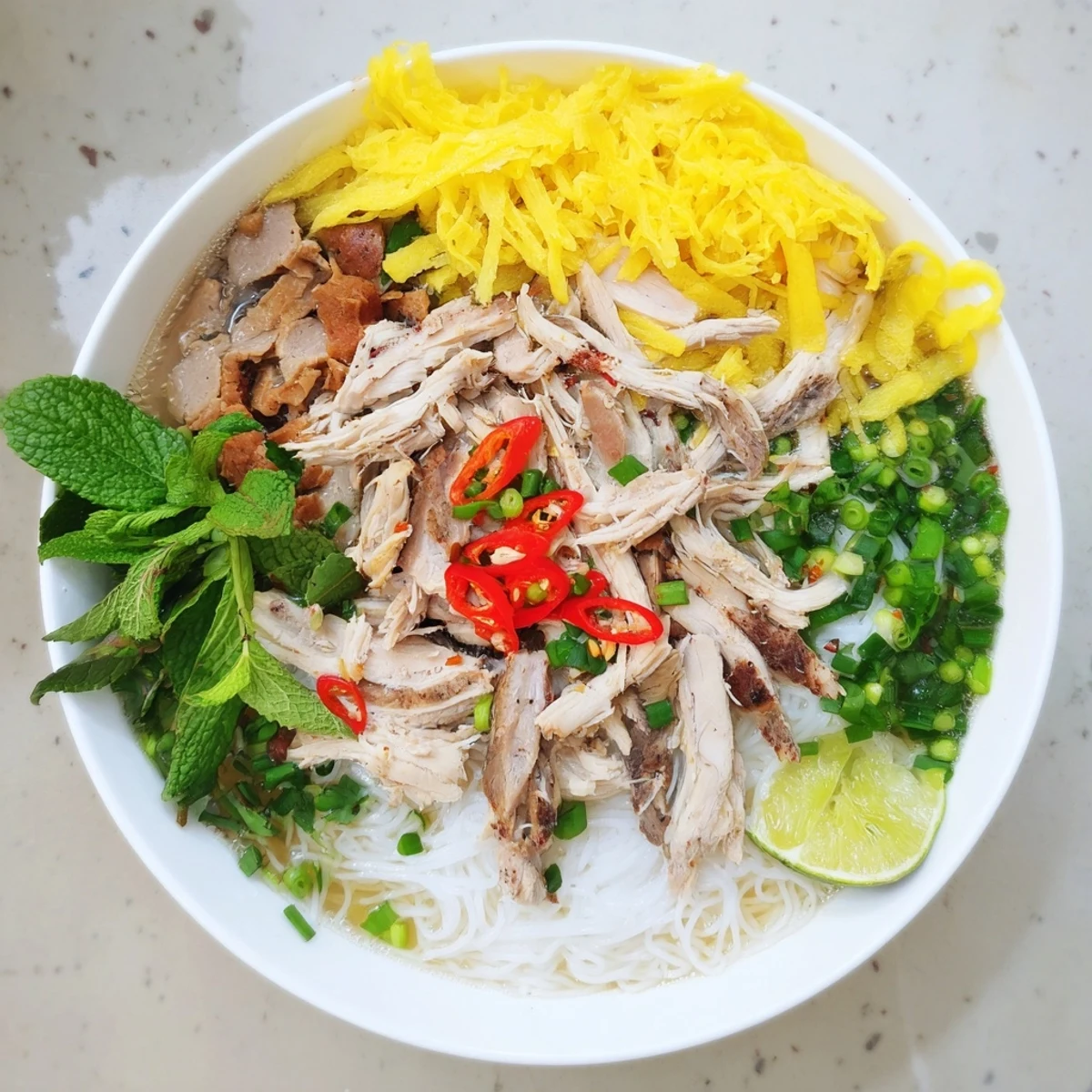 Steaming bowl of Bun Thang with shredded chicken, silky egg strips, and rice noodles in clear broth.  