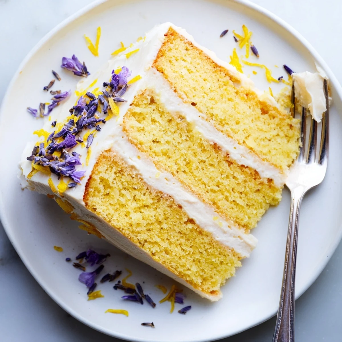 The London Fog Cake with Earl Grey & Lavender sits elegantly on a marble stand, showcasing fluffy layers and delicate lemon zest garnish.
