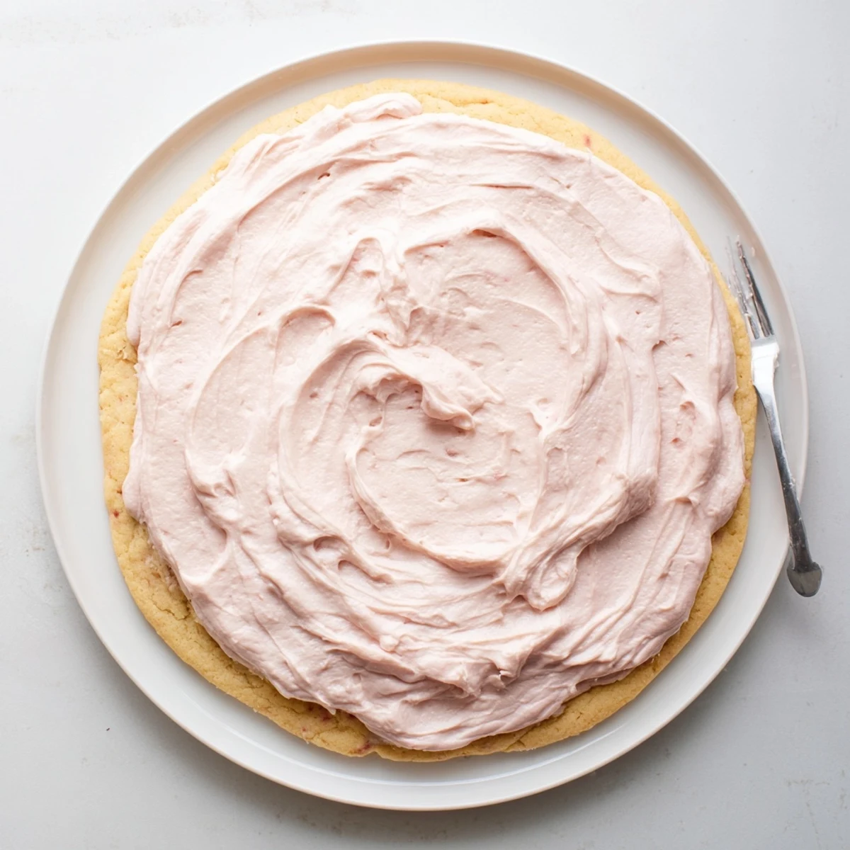 This image shows a soft, oversized sugar cookie topped with pink frosting, perfect for a bakery-style dessert or snack.