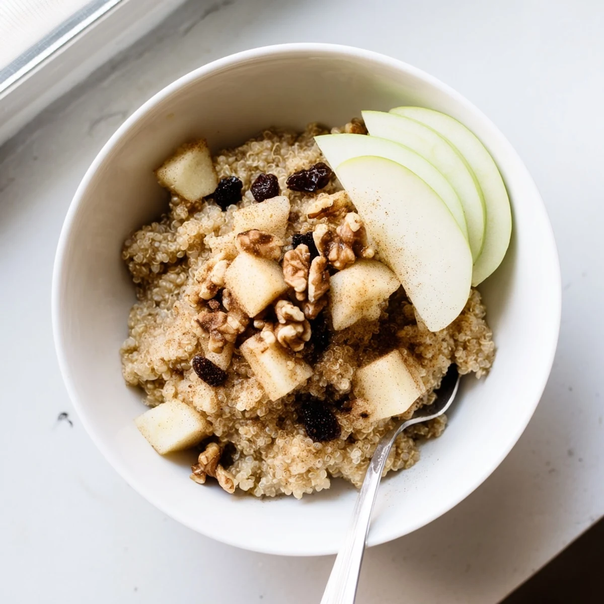 Steaming bowl of Healthy Quinoa Apple Breakfast topped with chopped walnuts and warm cinnamon spices.
