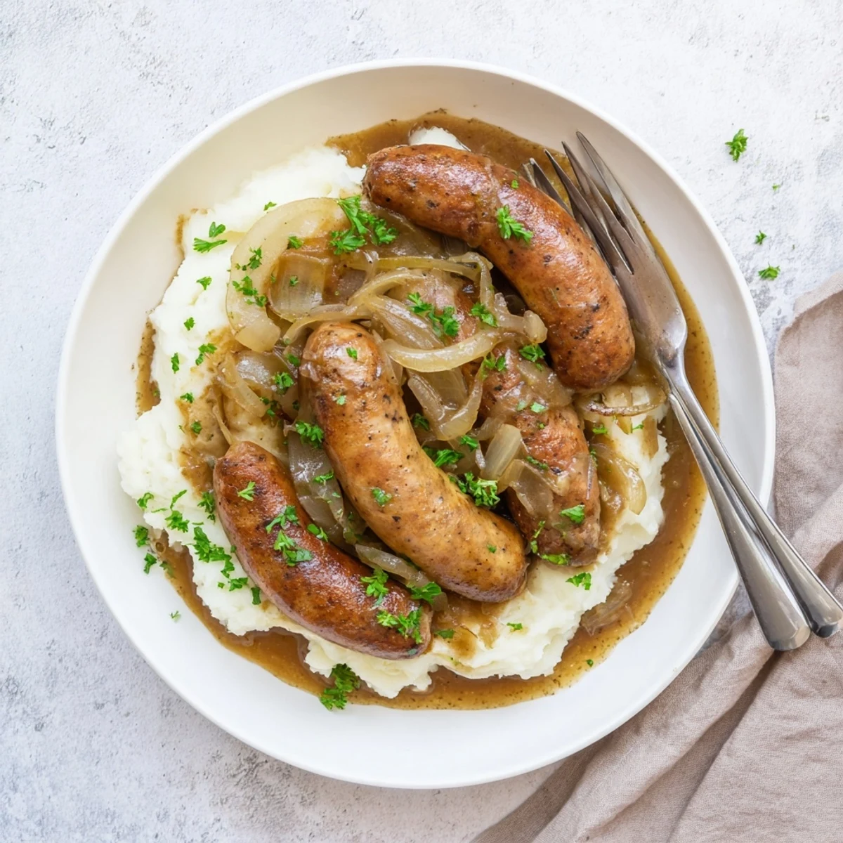 Juicy sausages simmered in rich onion gravy served over creamy mashed potatoes with parsley.