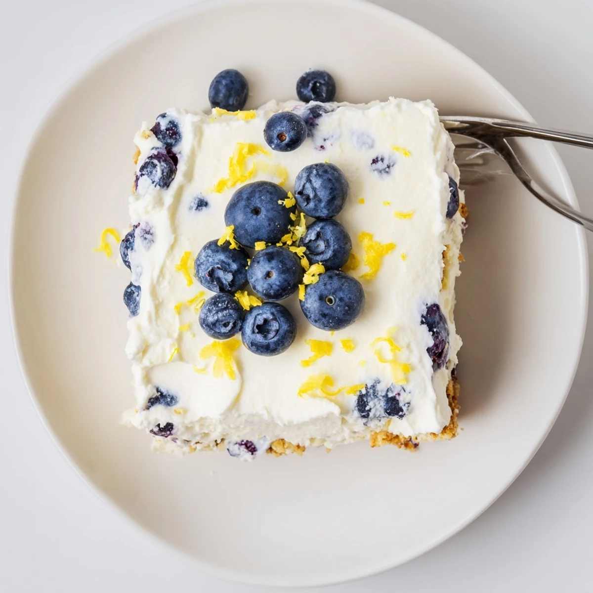 No-bake lemon blueberry cream cake garnished with whipped cream and lemon zest on a serving plate.