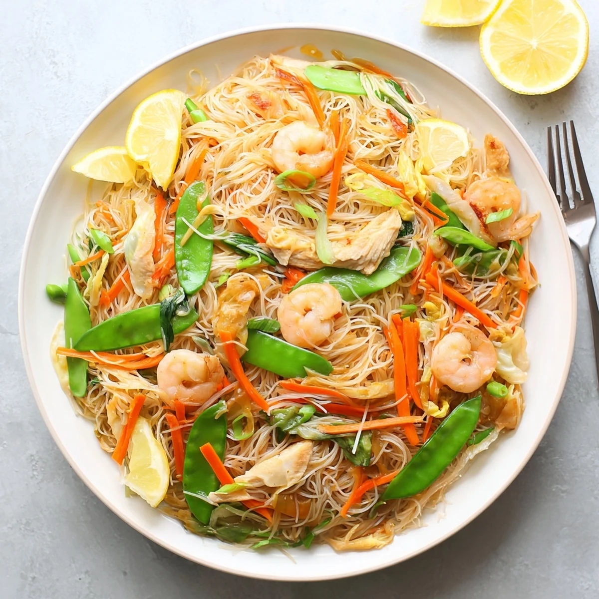 Golden traditional Pancit Bihon stir-fry topped with fresh scallions and calamansi wedges on a white serving plate