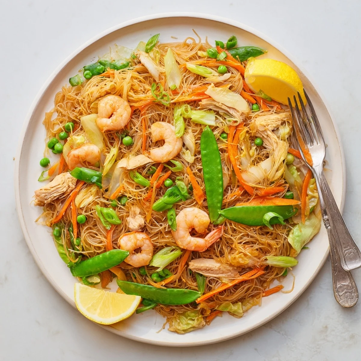Steaming plate of traditional Pancit Bihon featuring tender rice noodles with colorful julienned carrots and green cabbage