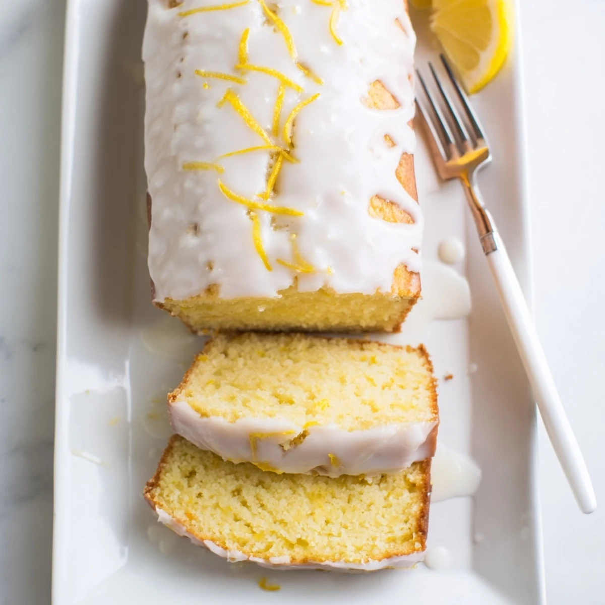 Moist lemon loaf cake drizzled with tangy citrus glaze on a white serving plate