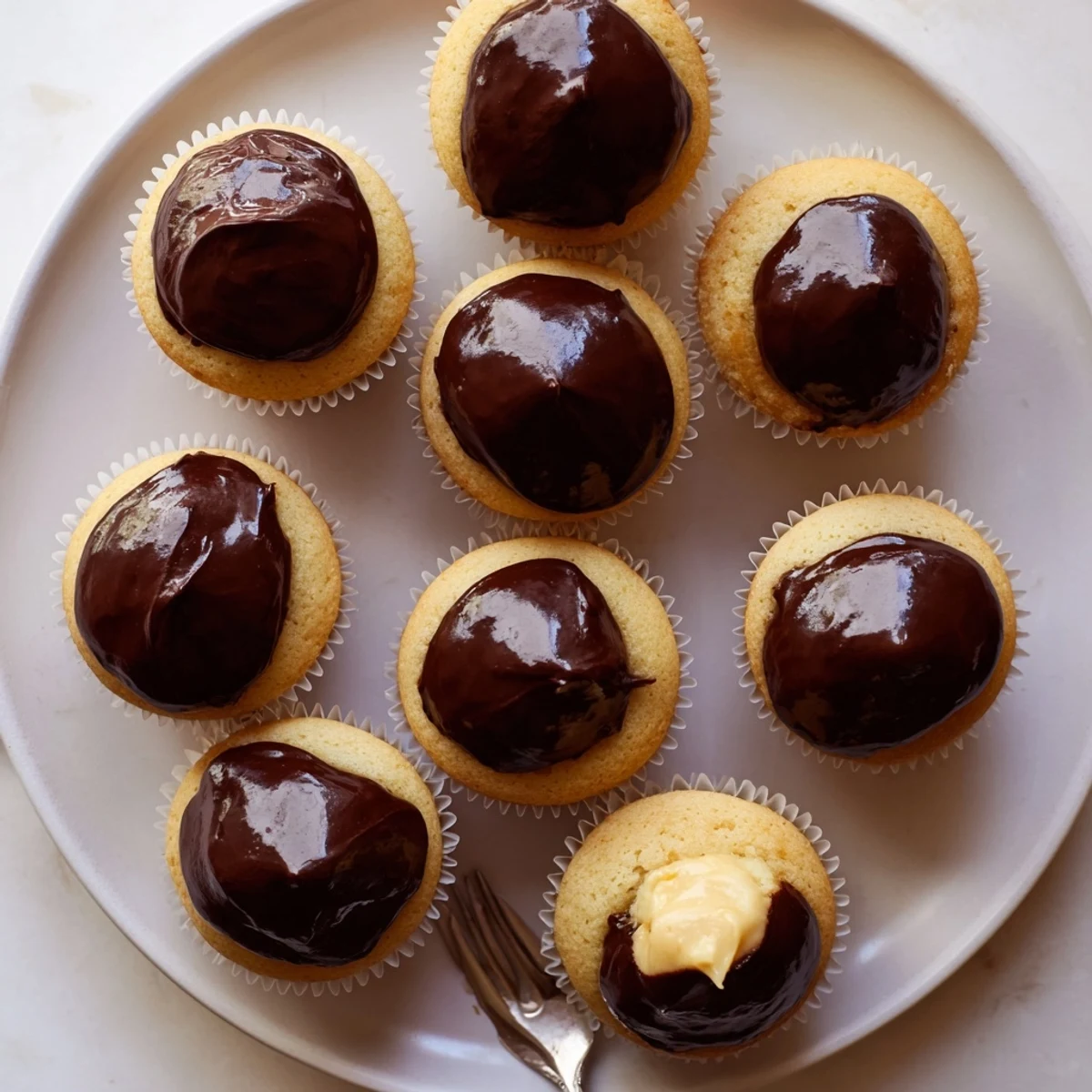 Classic Boston cream pie cupcakes featuring smooth vanilla custard centers dripping with rich semi-sweet chocolate topping