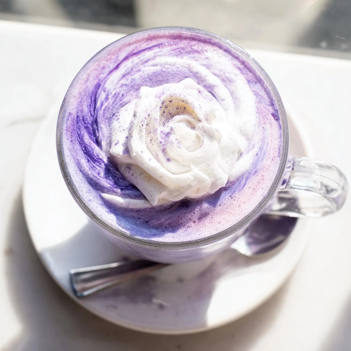 Creamy purple ube latte topped with whipped cream and purple yam flakes in a glass