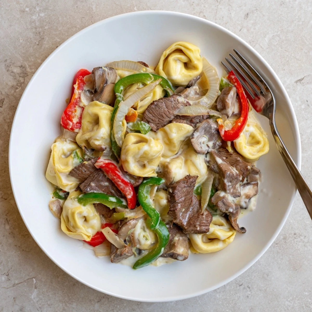 Hearty Crock Pot Cheesesteak Tortellini bowl topped with melted mozzarella and fresh chopped parsley