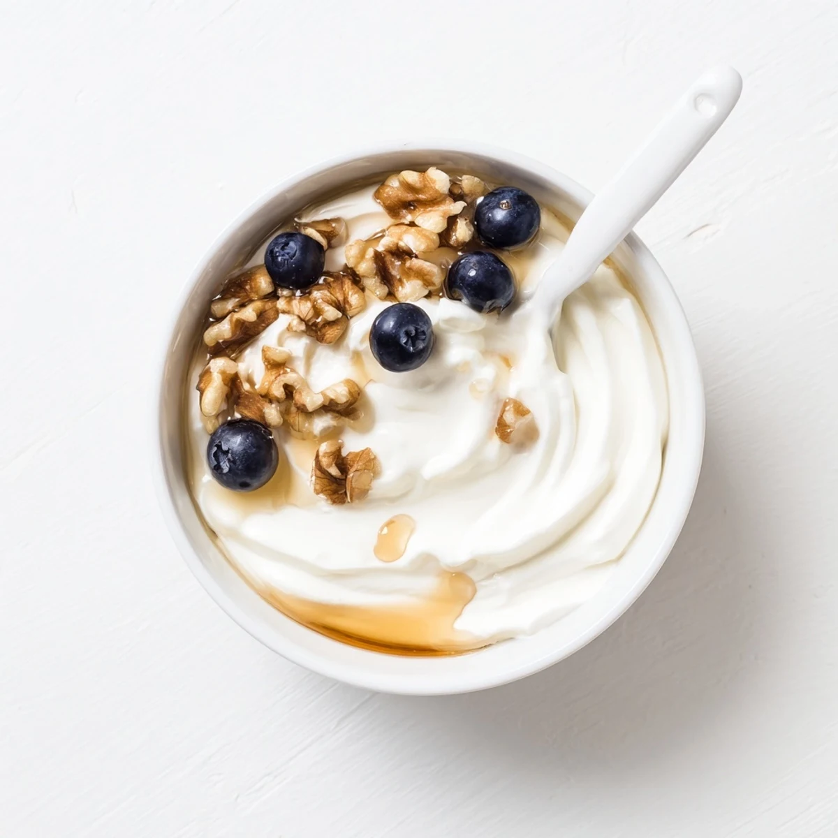 Thick strained Greek yogurt spoon drizzling golden honey over granola and sliced strawberries