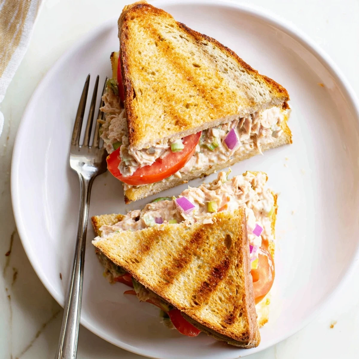 Hot open-faced tuna melt sandwich featuring savory tuna salad topped with melted tomato and cheese