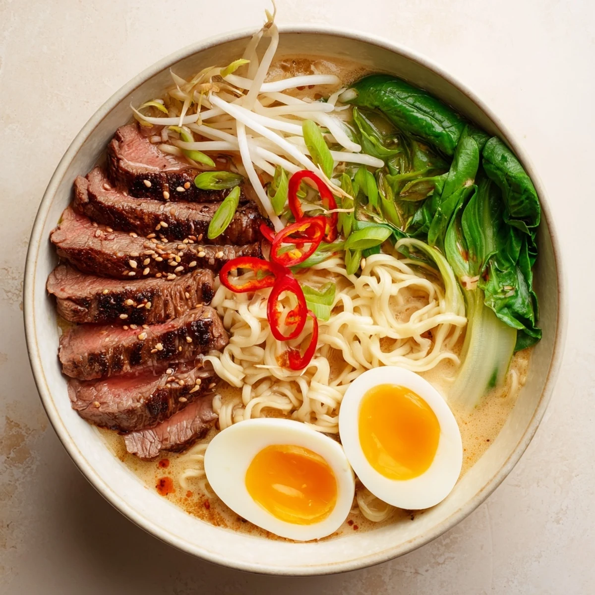 Steaming bowl of spicy beef ramen with creamy garlic sauce, soft-boiled egg, and fresh green onions