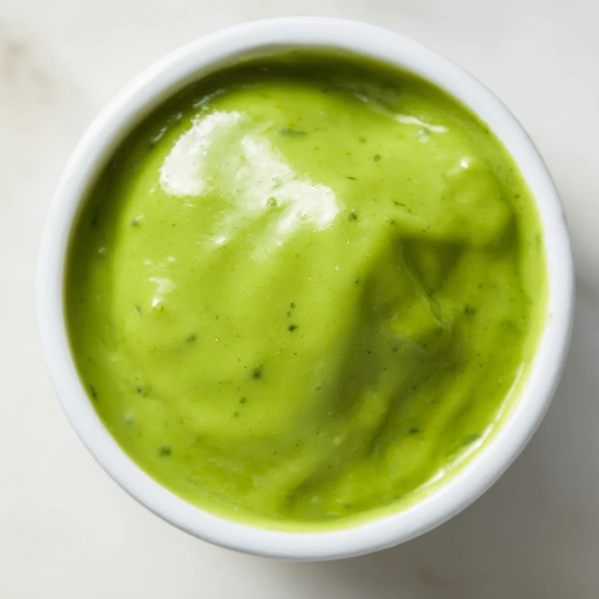 Creamy Peruvian green sauce aji verde drizzled over grilled chicken in a rustic white bowl