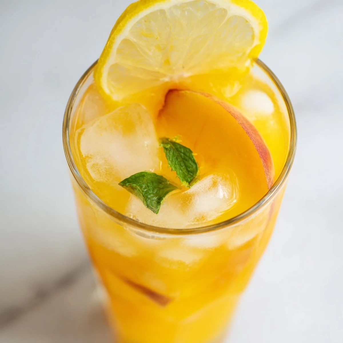 Golden fresh peach lemonade with floating peach slices, lemon wheels, and ice cubes in a tall glass