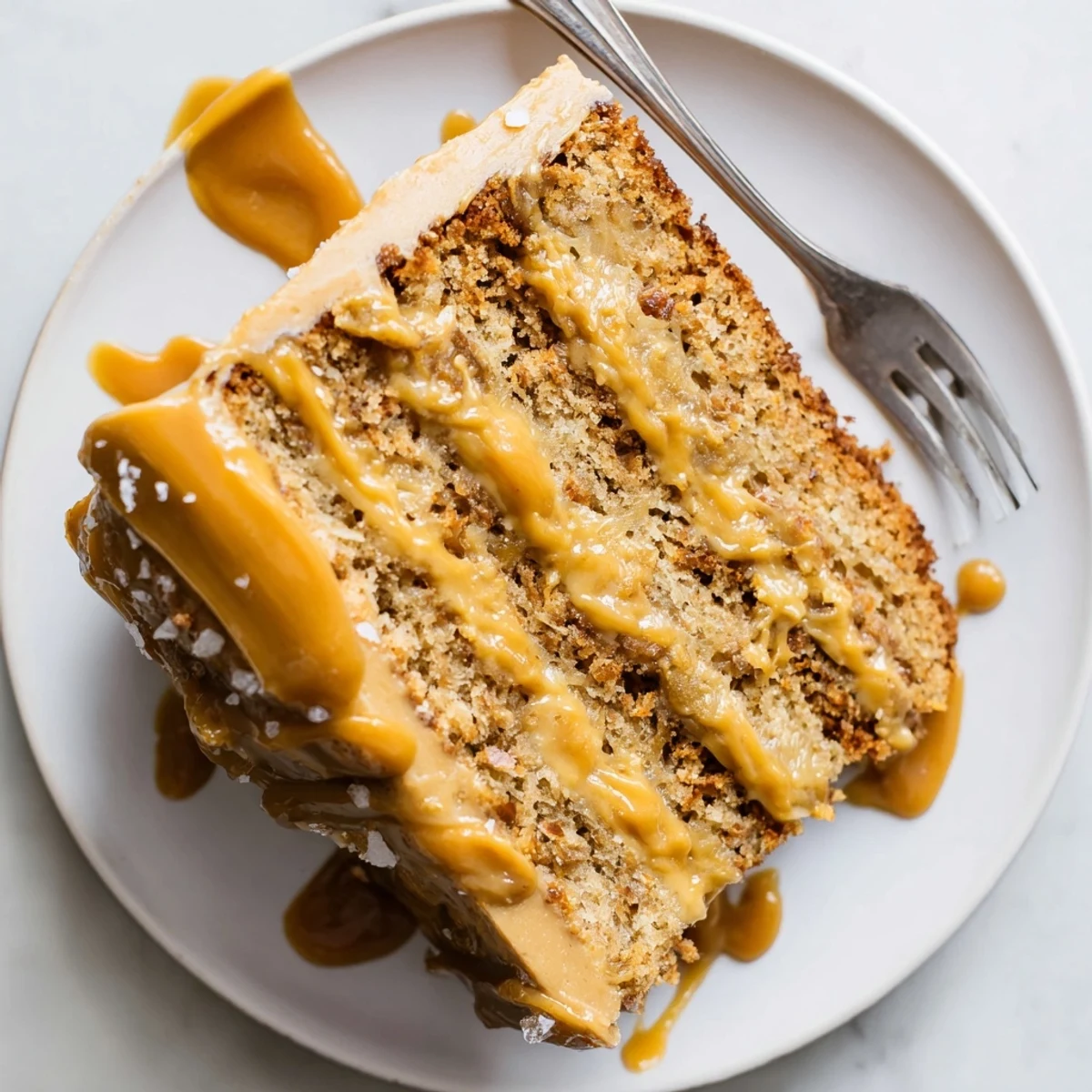 Slice of salted caramel brown butter banana cake plated with caramel pooling beneath on white plate