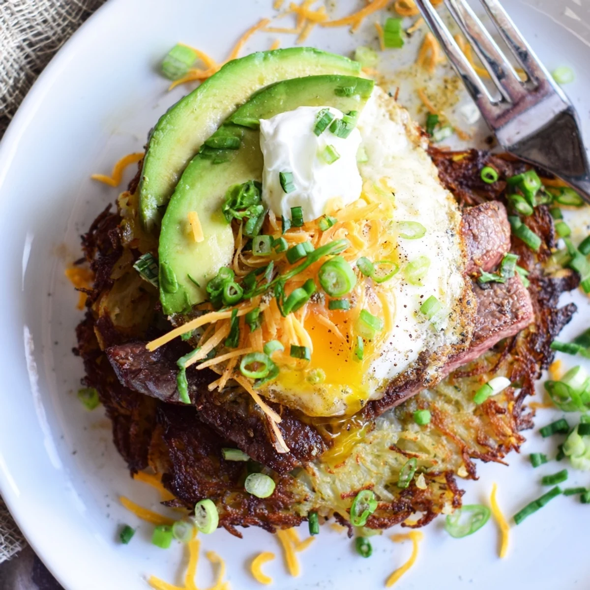 Savory brunch plate: Loaded Steak Egg Hash Brown Stacks Recipe garnished with avocado