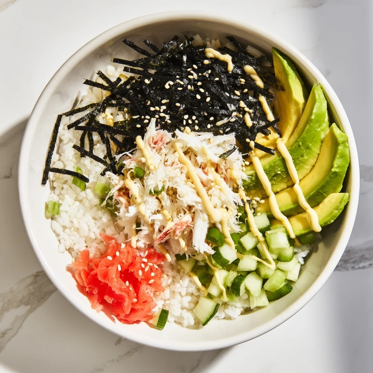 Deconstructed California roll sushi bowls featuring seasoned rice, imitation crab, avocado, and cucumber topped with spicy mayo and sesame seeds