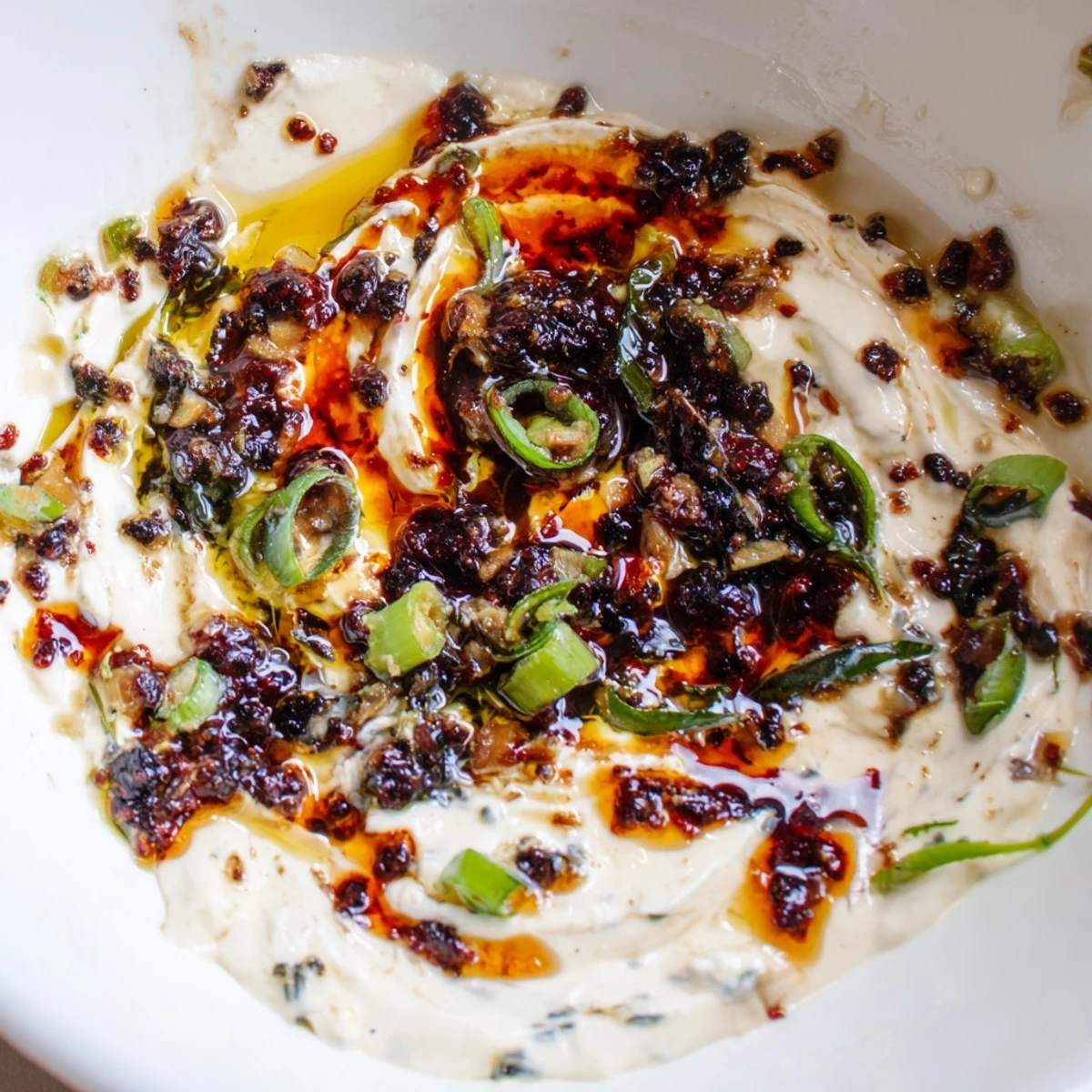 Vibrant charred scallion and chili crisp dip with glossy red oil drizzled over a velvety creamy base