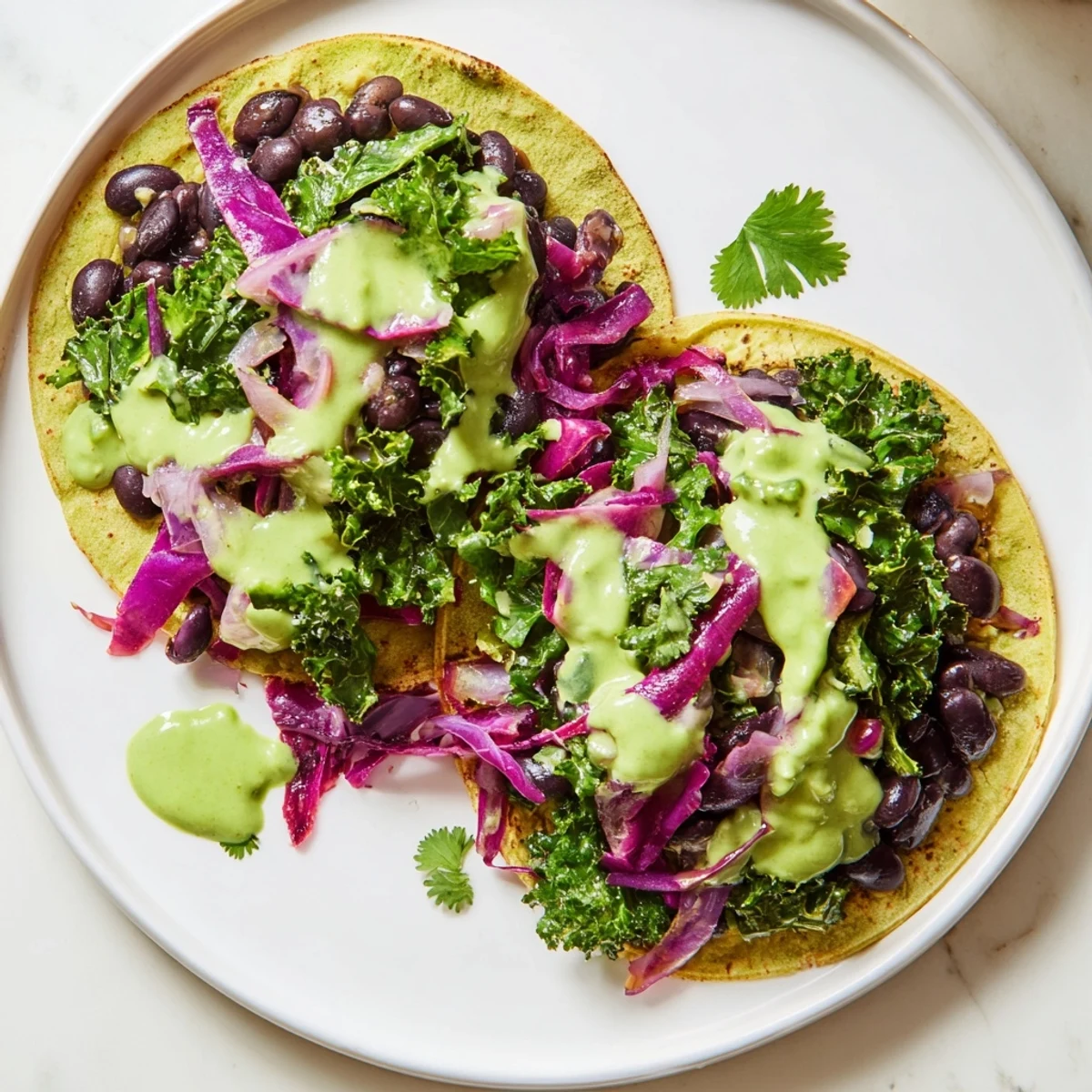 Smoky black bean kale tacos drizzled with creamy green sauce on corn tortillas