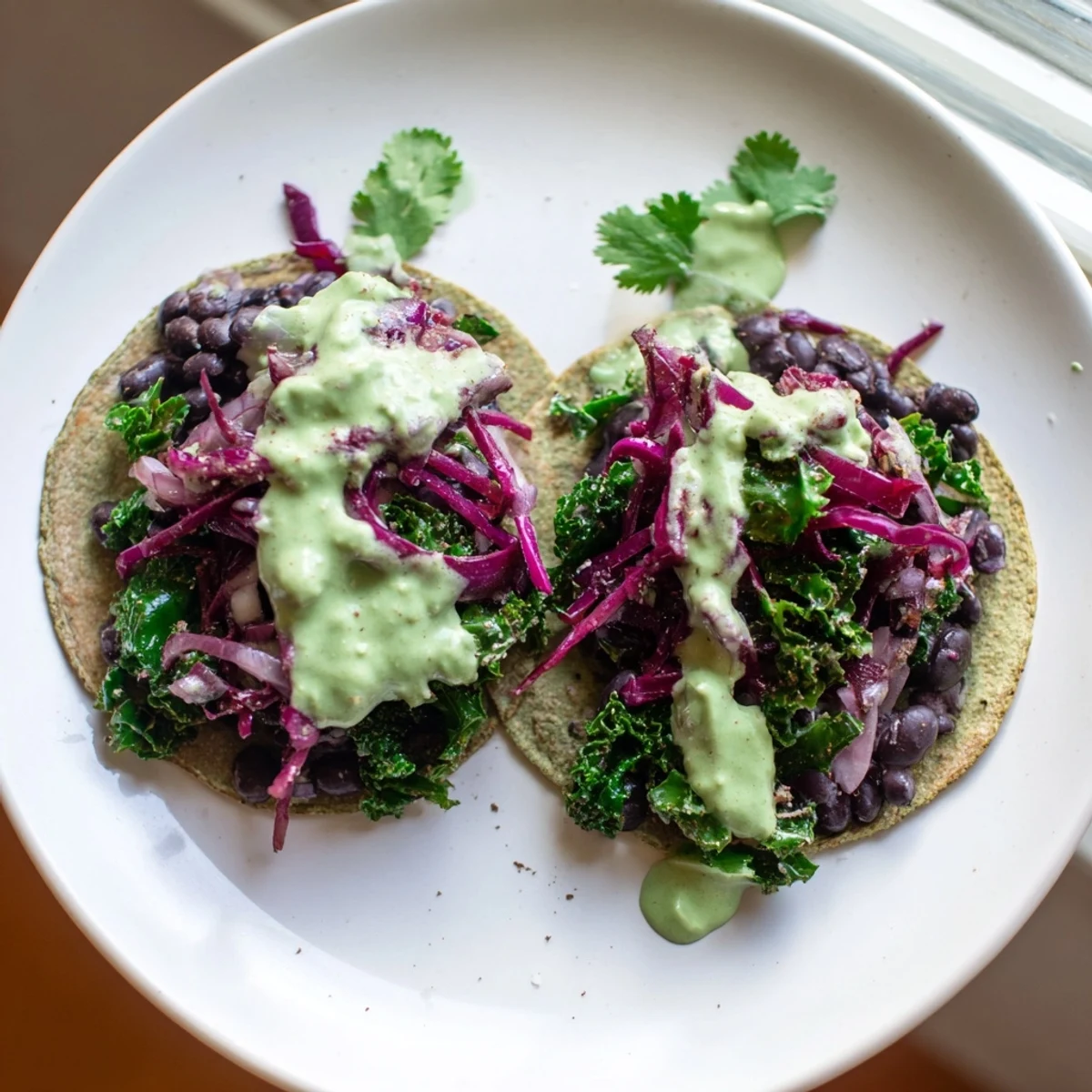 Warm smoky black bean kale tacos topped with fresh cabbage and herby avocado sauce