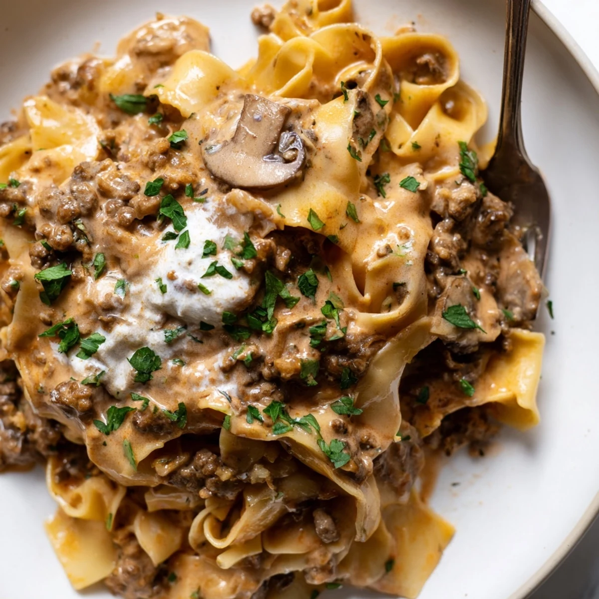 Warm bowl of hamburger stroganoff coated in velvety sauce topped with chopped parsley