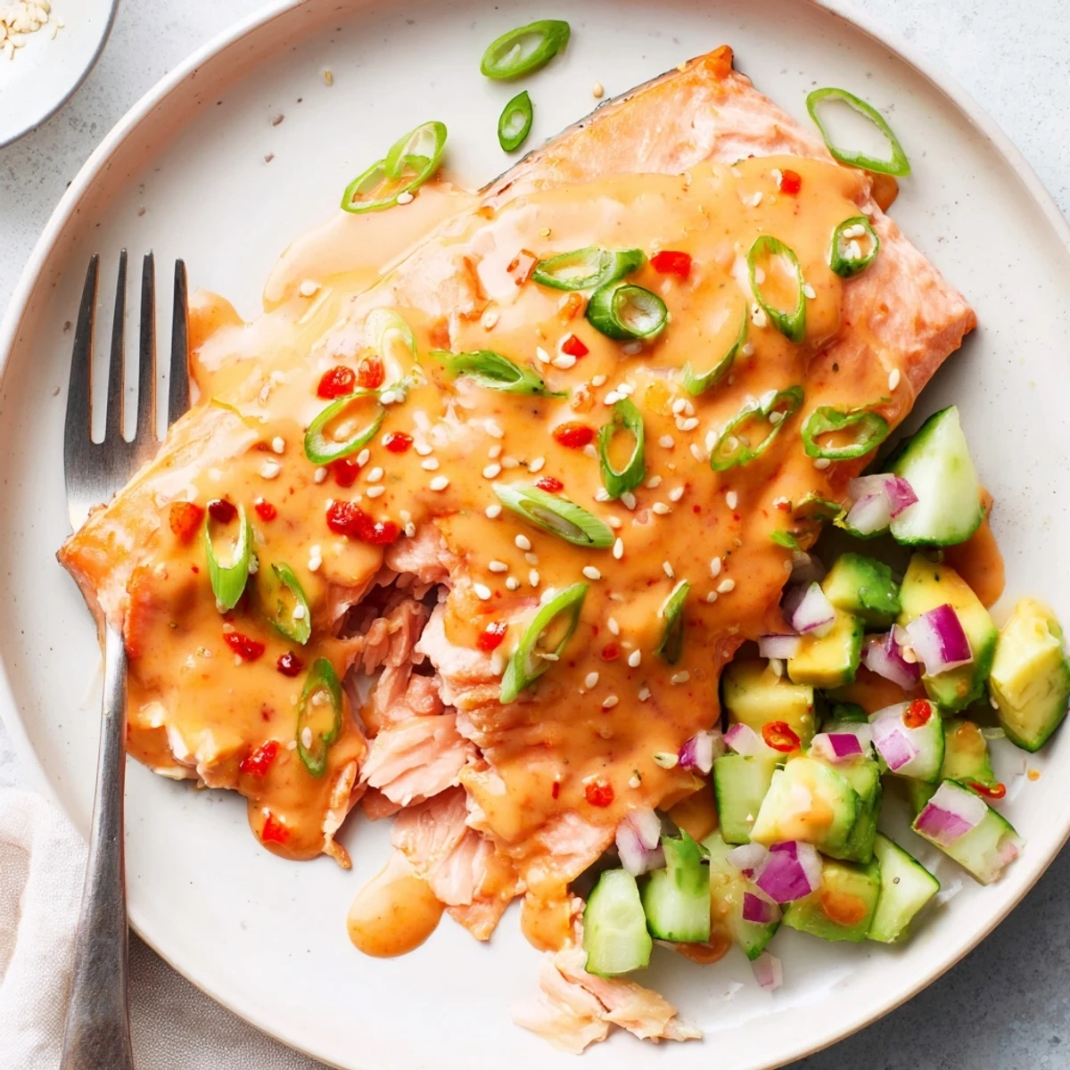 Crispy baked Bang Bang Salmon drizzled with spicy cream sauce and fresh avocado cucumber salsa.
