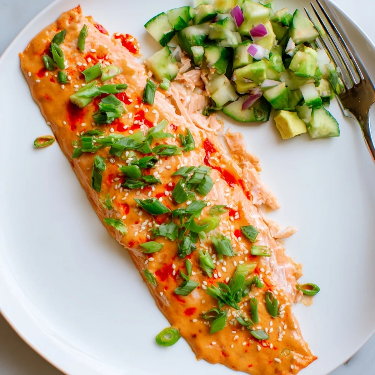 Tender flaky Bang Bang Salmon glazed in sweet chili mayo served beside vibrant green avocado cucumber salsa.