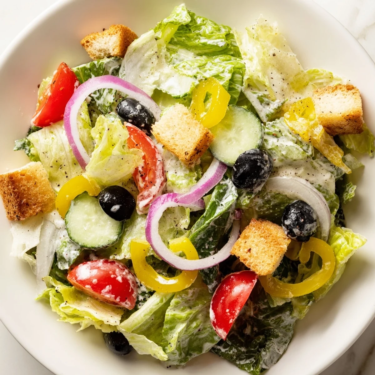 Colorful Olive Garden Salad tossed with romaine, black olives, and garlic croutons